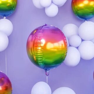 Grote regenboogkleurige folie ballon met daarachter paarse ballonnen