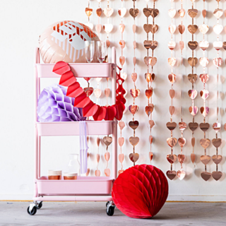 roze karretje met ballonnen en honeycombs staat voor een rose gouden backdrop met hartjes