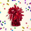 Rood gewichtje voor ballonnen van 130 gram met franjes op een lichtgele achtergrond met confetti