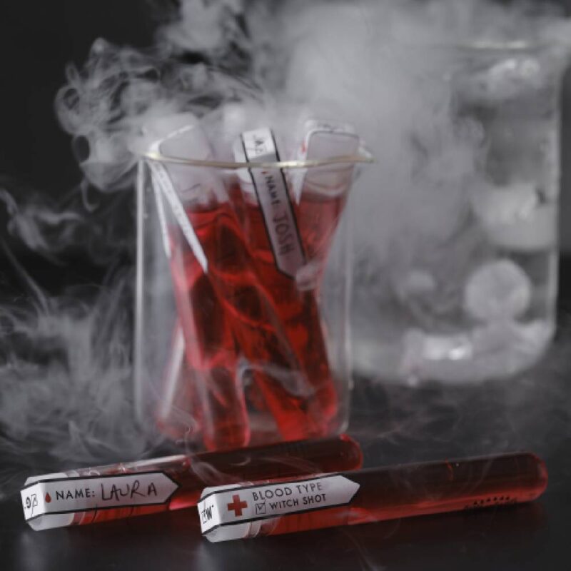 Glas met daarin reageerbuisjes met rode vloeistof en rook