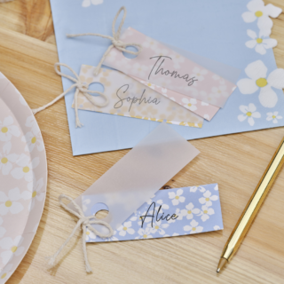 Pastel naamkaartjes met velijnpapier liggen op een houten tafel naast een gouden pen