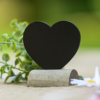 Krijtbord in de vorm van een hartje in een houten standaard staat op tafel naast madeliefjes en eucalyptus