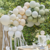 Ballonnenboog met streamers in het sage, perzik en wit hangt voor een boom en achter een houten tafel
