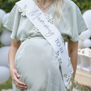 Zwangere vrouw in lichtgroene jurk draagt een sagegroene sjepr met bladeren en de tekst mummy to be