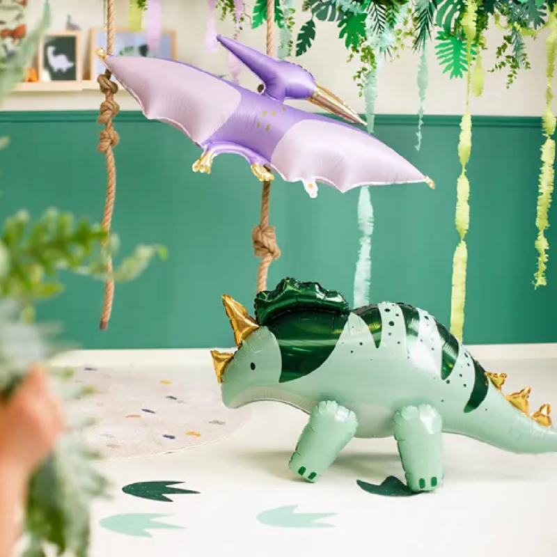 Groene folieballon van een dino en een paarse folieballon van een dino staan in een groene kamer