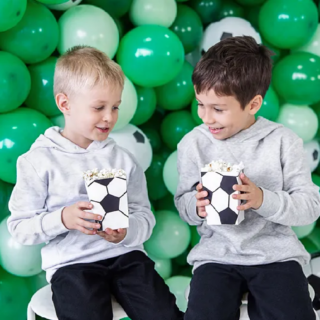 Twee jongens zitten voor een muur van groene ballonnen met een bakje bedrukt met een voetbal