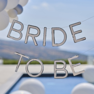 Zilveren slinger met de tekst bride to be hangt voor een zwembad met witte ballonnen