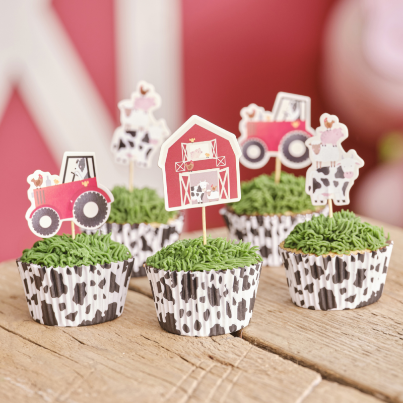 Cupcakes in een wikkel met koeienprint staan op een houten tafel en zijn versierd met cupcaketoppers met tractors en boerderijdieren erop