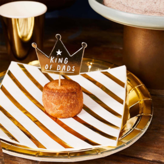 Gouden bordje met witte servet met strepen en een gebakje met hierin een cocktailprikker in de vorm van een kroon met de tekst king of dads