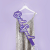 Paarse sjerp hangt over een zilveren glitter jurk aan een witte hangen voor een lila achtergrond
