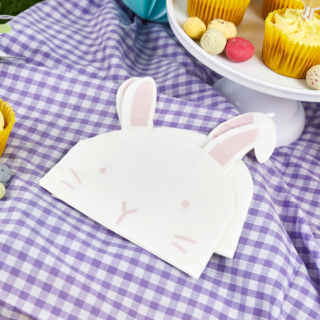 Servetten in de vorm van konijntjes liggen op een wit en paars geblokt tafelkleed met een plateau gevuld met cupcakes