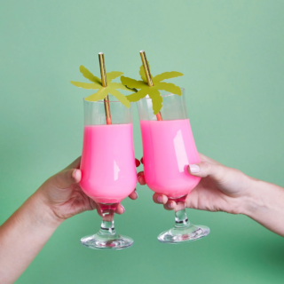 Er word geproost met glazen met roze drinken voor een groene muur