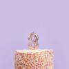 rose gouden taart kaars cijfer in een regenboog taart met spikkels voor een paarse muur