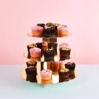 gouden standaard met drie verdiepingen gevuld met chocolade en roze cupcakes staat voor een roze en blauwe muur