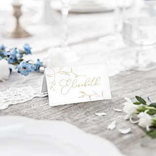 wit tafelkaartje met gouden blad staat op een grijze houten tafel naast blauwe bloemen