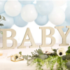 houten letters baby onder een wit met blauwe ballonnenboog naast groene bladeren