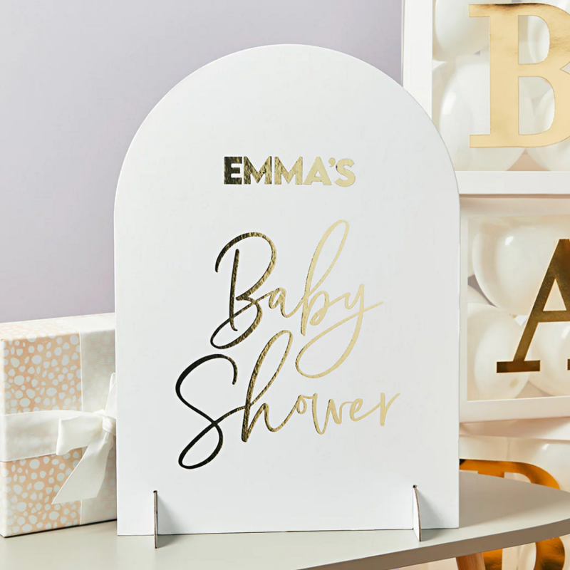 wit bord met gouden tekst emma's babyshower staat voor gouden en witte blokken op een houten tafel