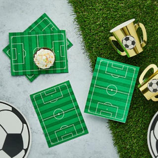 Servetten in de vorm van een groen voetbalveld liggen op een grasmat naast gouden bekers en een cupcake