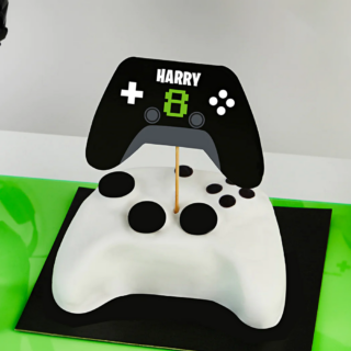 personaliseerbare taart topper in de vorm van een zwarte controller met stickervellen in het groen en wit in een witte taart in de vorm van een playstation controller