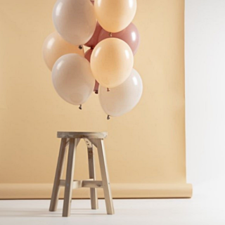 ballonnen in perzikkleur, nude en oud roze hangen voor een perzikkleurige backdrop aan een houten kruk