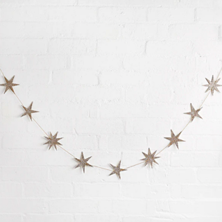 Sterrenslinger met gouden glittersterren hangt voor een witte muur met bakstenen