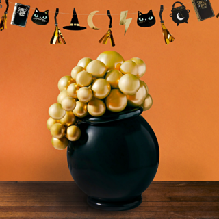 Zwarte heksenketel met gouden bubbels staat voor een oranje muur op een houten tafel