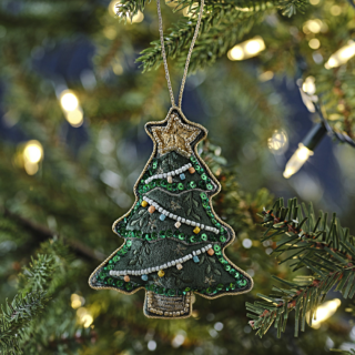 Stoffen hanger in de vorm van een groene kerstboom met gouden ster en kralen hangt in een boom met een lampjesslinger