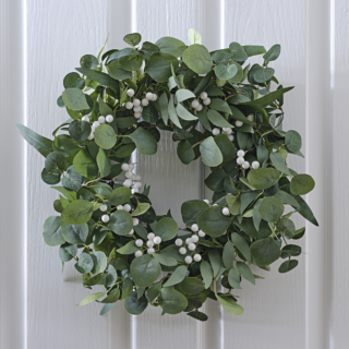 Krans met eucalyptusbladeren en witte besjes hangt aan een witte, houten deur