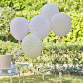 Pastel ballonnen in het roze, perzik en geel bedrukt met witte stippen en bloemen staarten hangen in de tuin voor een roze taart