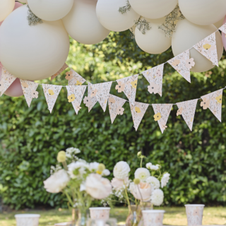 Vlaggenlijn met roze en gele bloemen in pasteltinten hangt onder een roze ballonnen boog in een tuin