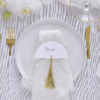 Wit tafelkaartje met een gouden tassel ligt op een witte, stoffen servet
