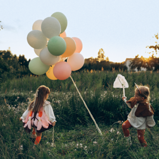 twee meisjes met verkleedkleren staan in een veld met pastel ballonnen