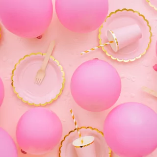 roze ballonnen liggen op een roze kleed met roze met gouden bekers en bordjes