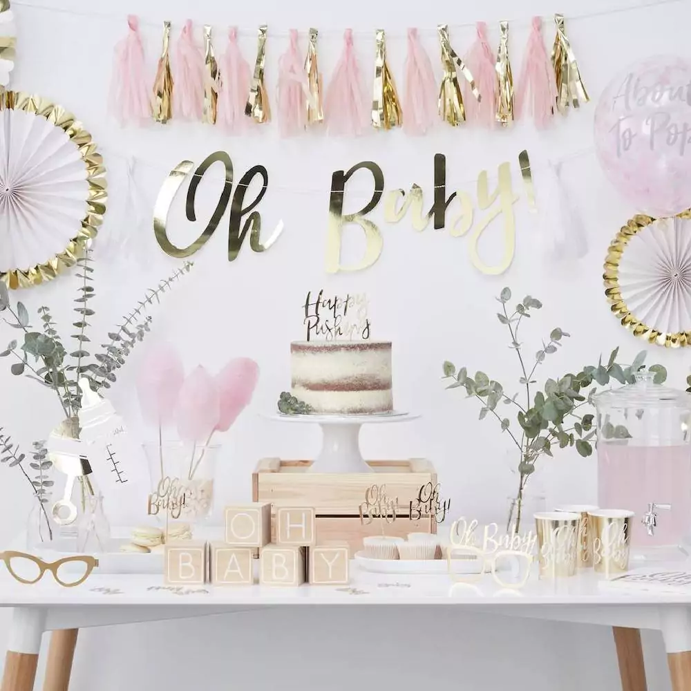 Babyshower hapjes tafel met taart en cupcakes en aan de muur waaiers een letterbanner en een tasselslinger