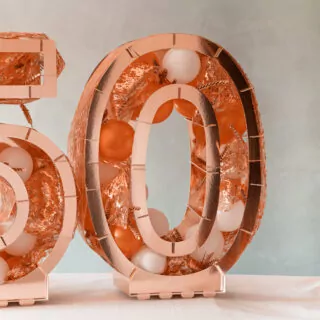 rose goudkleurig ballonstandaard in de vorm van een 0 gevuld met ballonnen en decoratie