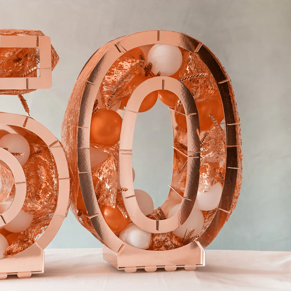 rose goudkleurig ballonstandaard in de vorm van een 0 gevuld met ballonnen en decoratie