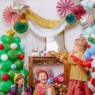Drie kinderen in een kamer met ballonnen kerstboom waaiers en slingers
