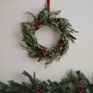 Kerstkrans aan rood lint met rode besjes met daaronder een kerstslinger