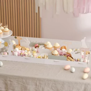 Tafel met een witte hapjesplank met konijntjes en wortels, versierd met paaseieren, marshmallows en macarons