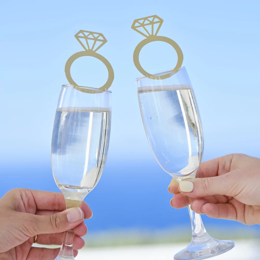 Champagneglazen worden vastgehouden voor een blauwe zee en zijn versierd met een gouden drankjestopper in de vorm van een ring