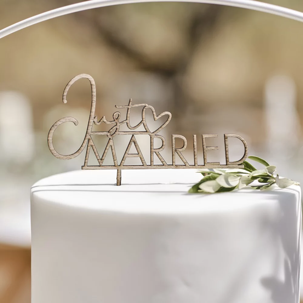 Houten taarttopper met de tekst just married zit in een witte taart versierd met bladgroen