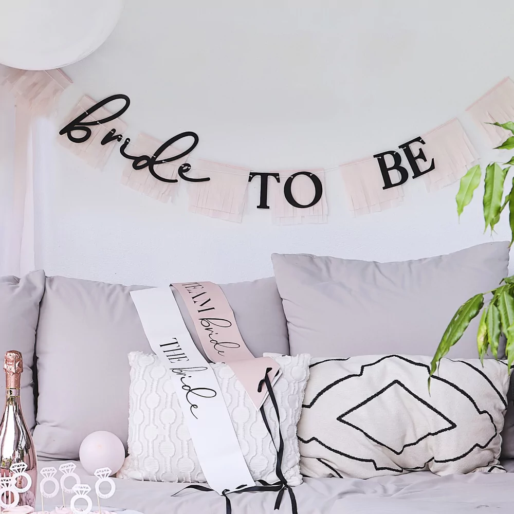 Slinger met roze franjes en de zwarte tekst bride to be hangt voor een roze ballonnenboog en een bank met beige kussens