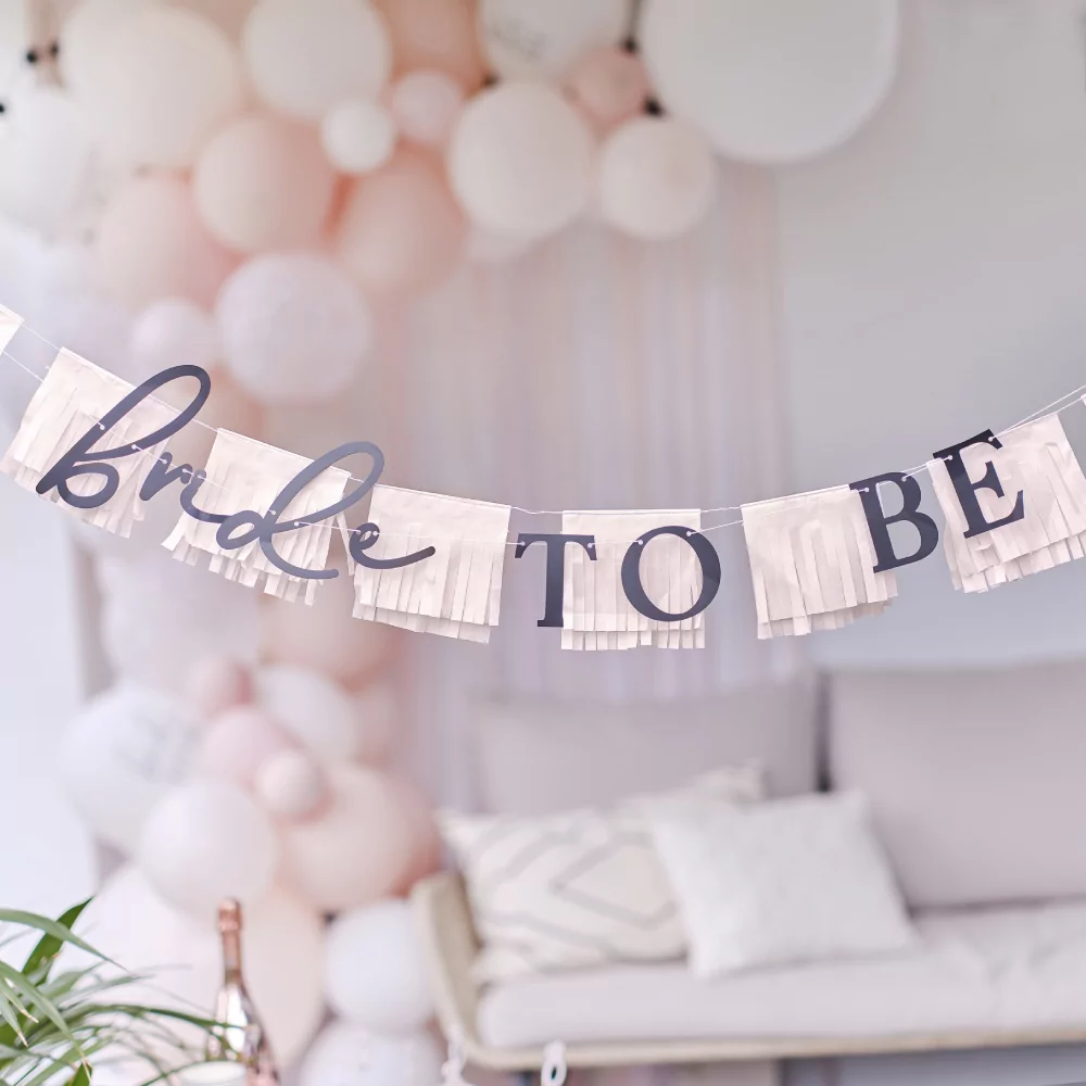 Slinger met roze franjes en de zwarte tekst bride to be hangt voor een roze ballonnenboog en een bank met beige kussens