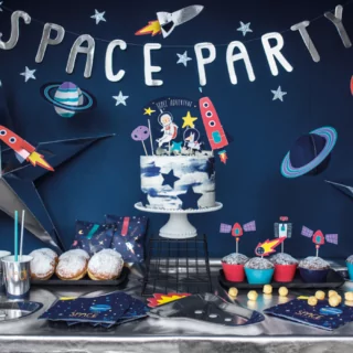 Tafel versierd met metallic zilver tafelkleed, donkerblauwe servetten met 'Space' erop, een wit met donkerblauwe taart en puddingbroodjes