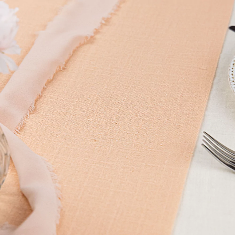 Rose tafelloper ligt op een witte tafel naast zilveren bestek en lichtroze lint