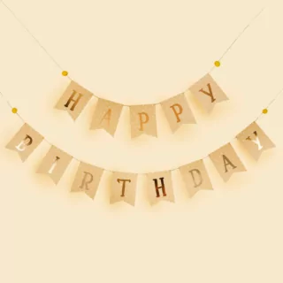 slinger met gele vlaggetjes en de gouden tekst happy birthday met witte stippen hangt voor een lichtgele achtergrond
