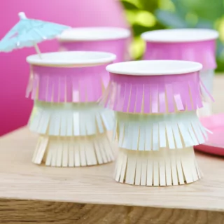 Papieren bekers met franje in het roze, groen en geel staan op een houten tafel voor een roze ballon