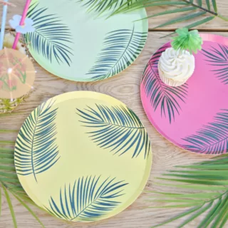 Papieren bordjes in het roze, groen en geel met groene palmbladeren liggen op een houten tafel