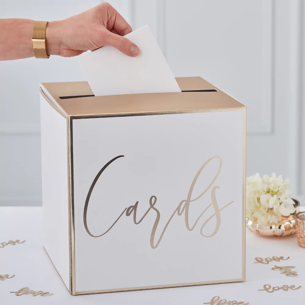 witte met gouden doos met hierop de tekst cards staat op een witte tafel naast rozen en gouden confetti