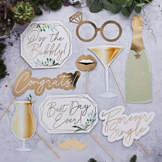 Photobooth props voor een bruiloft in het goud, groen en wit liggen op een marmeren ondergrond naast bladgroen